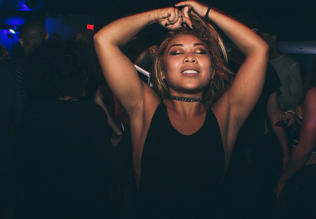 A dancer with their arms up under blue light at a HEAT event
